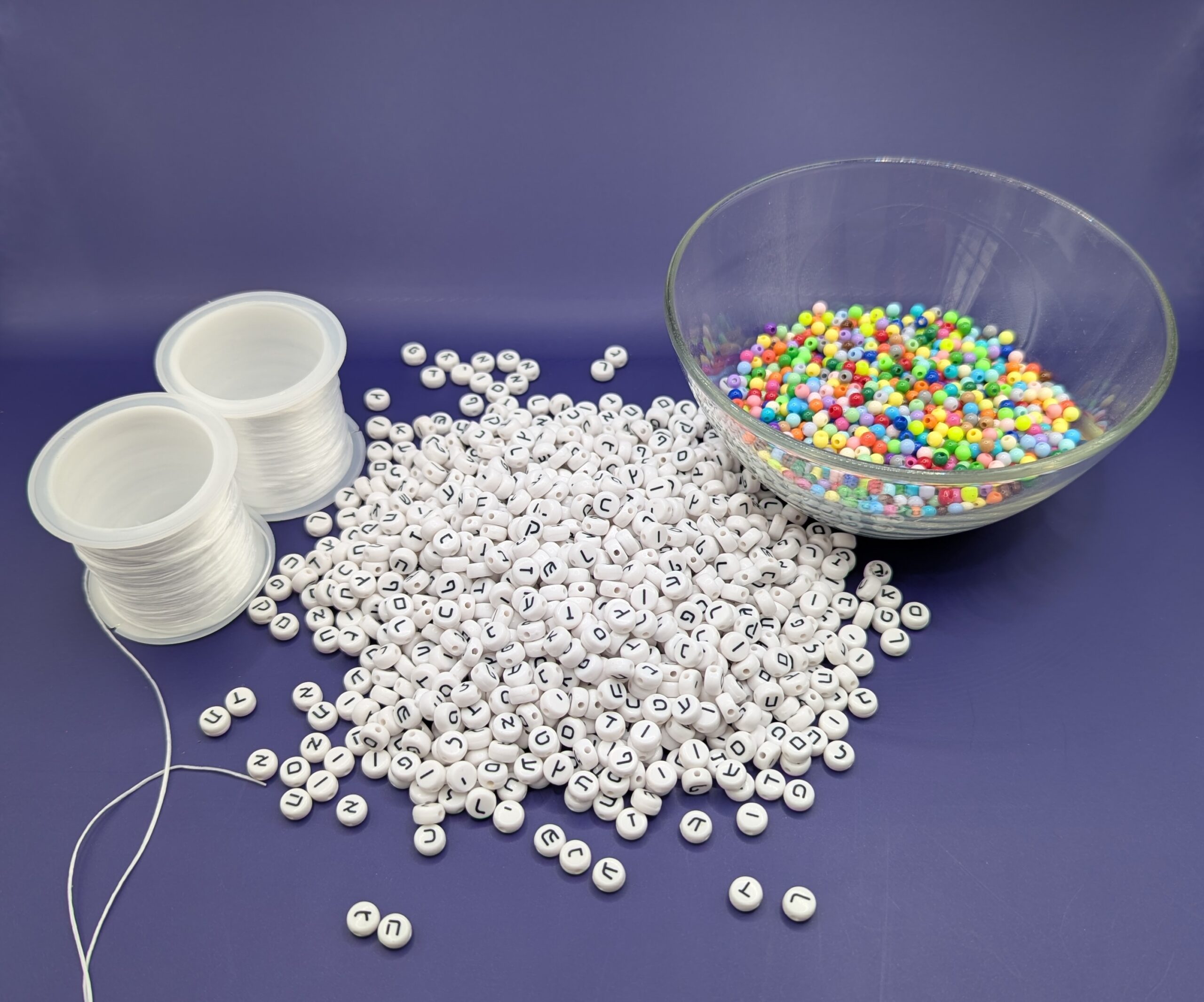 Two rolls of jewelry elastic, a pile of about 1000 plastic Hebrew beads, and a glass bowl of pastel filler beads.