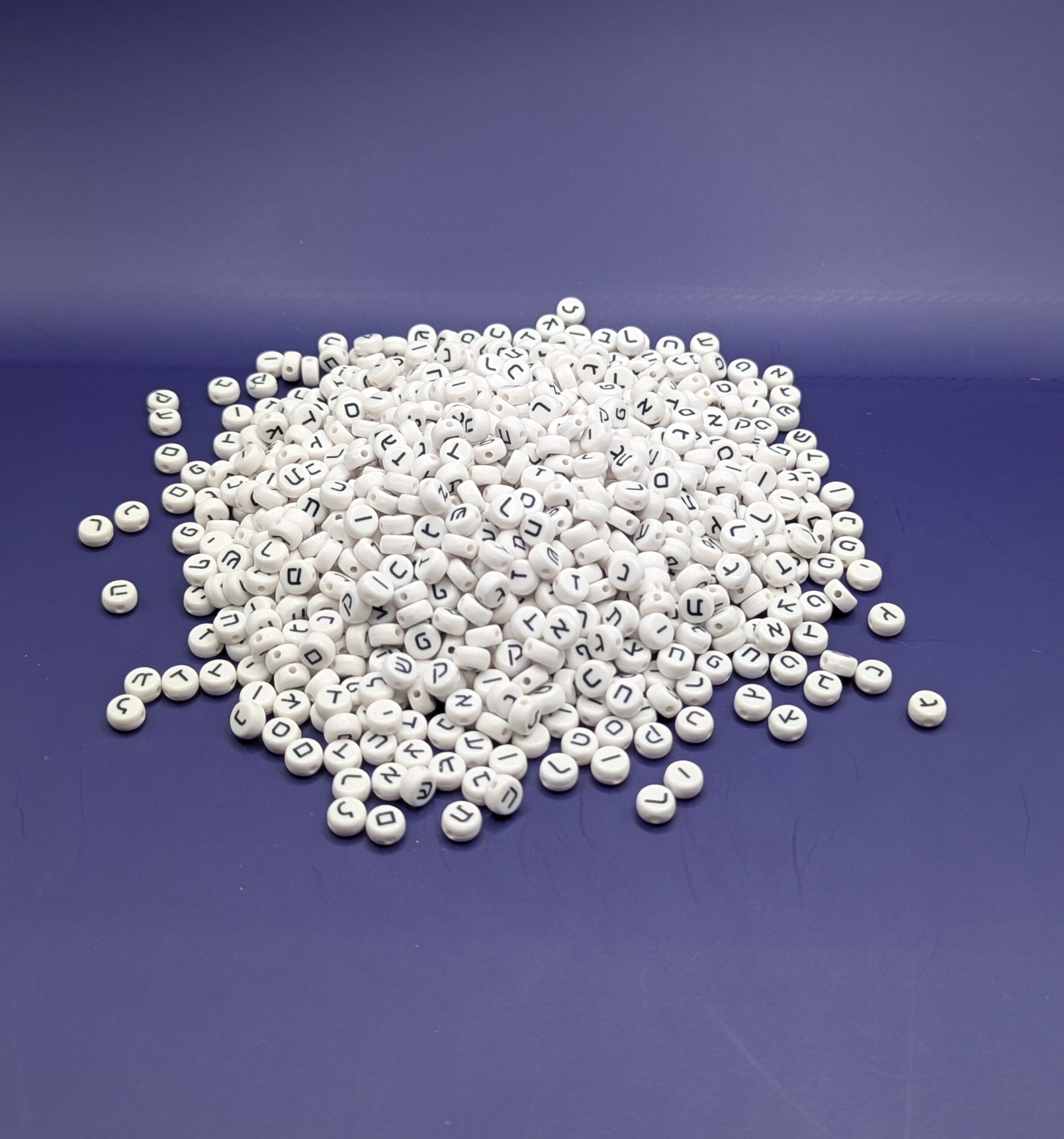 A pile of about 1000 white plastic Hebrew beads on a purple background