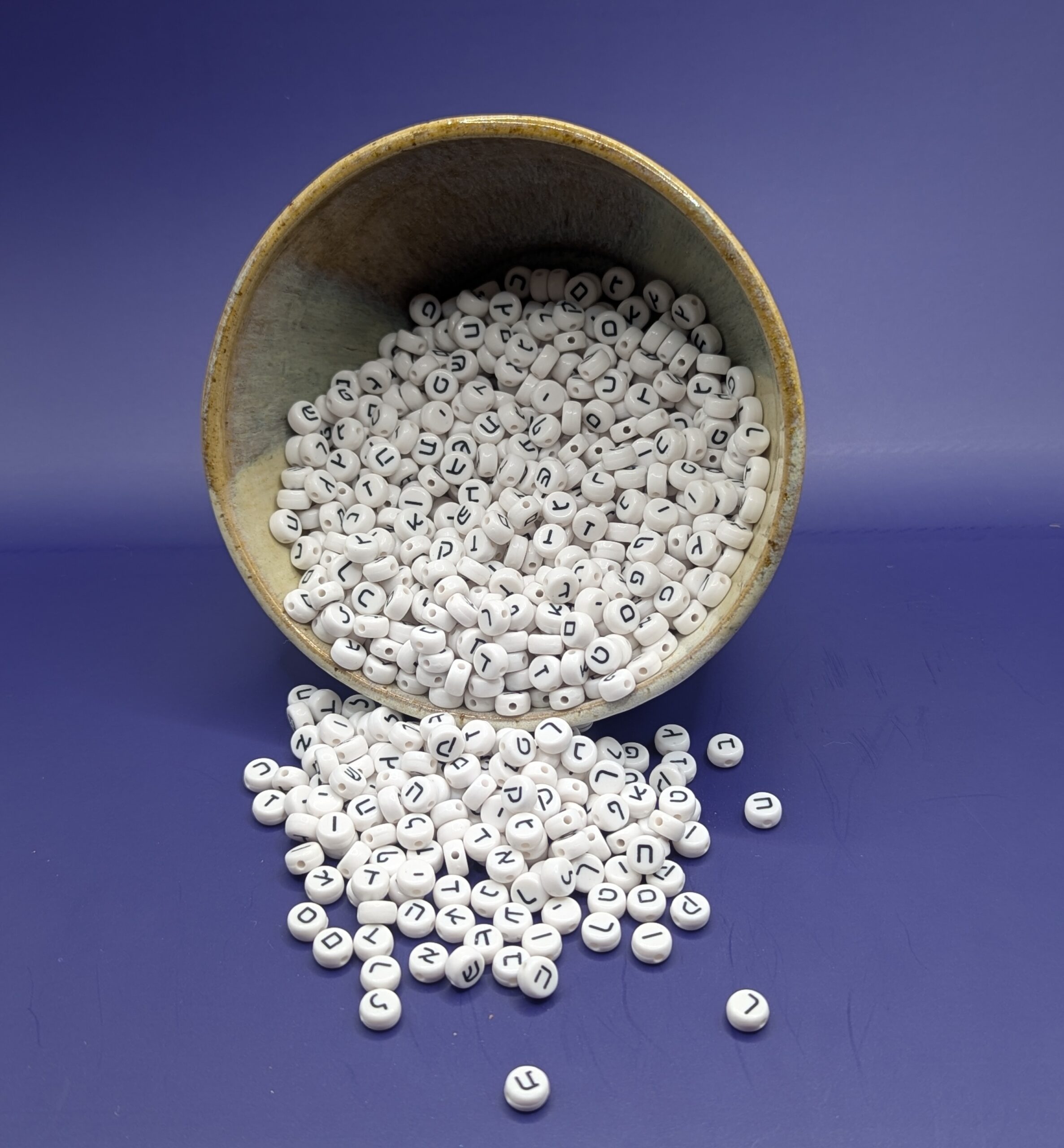 A pile of 1000 plastic Hebrew beads, spilling from a ceramic bowl.
