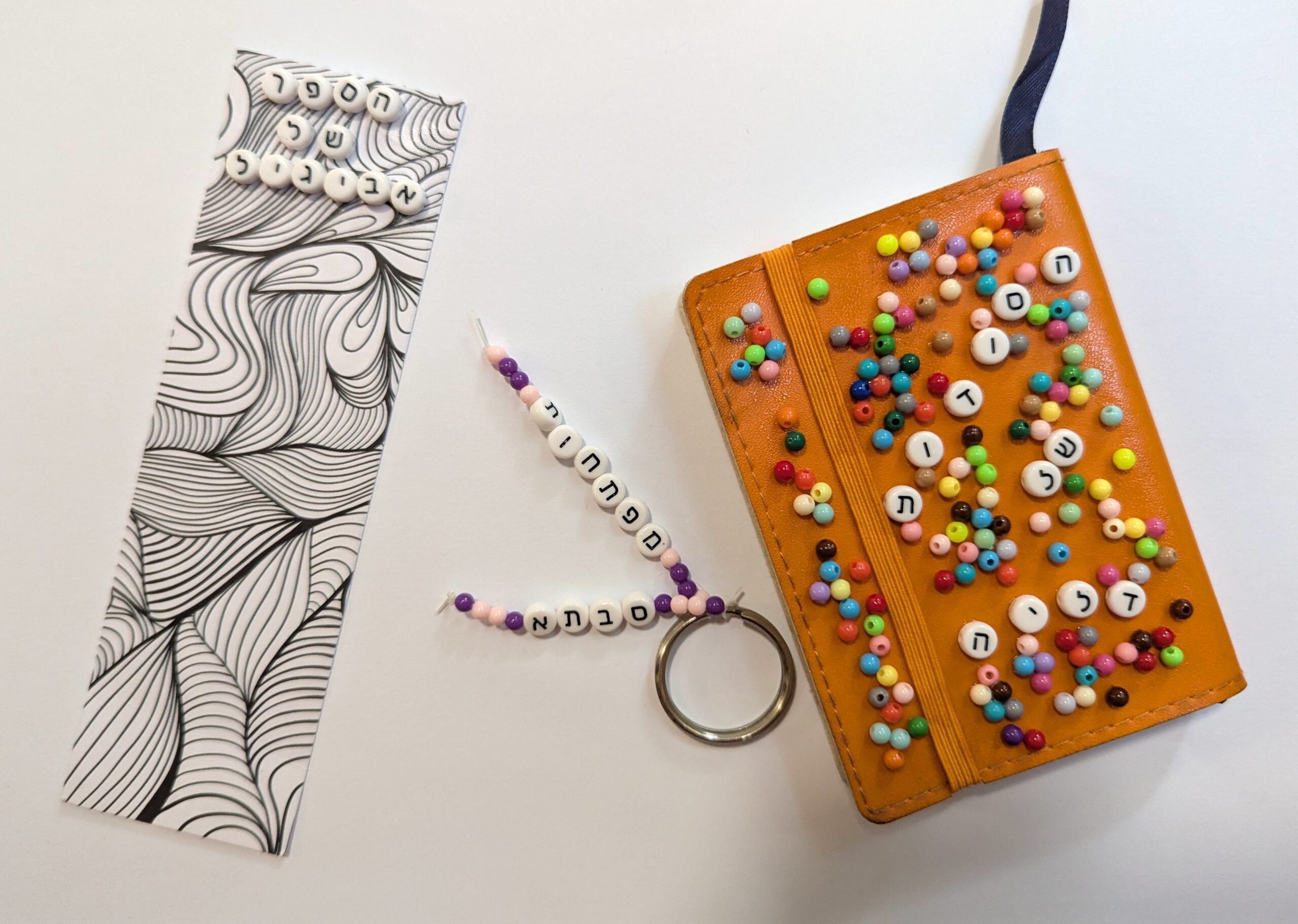 A bookmark, keychain, and notepad covered in Hebrew letter beads.
