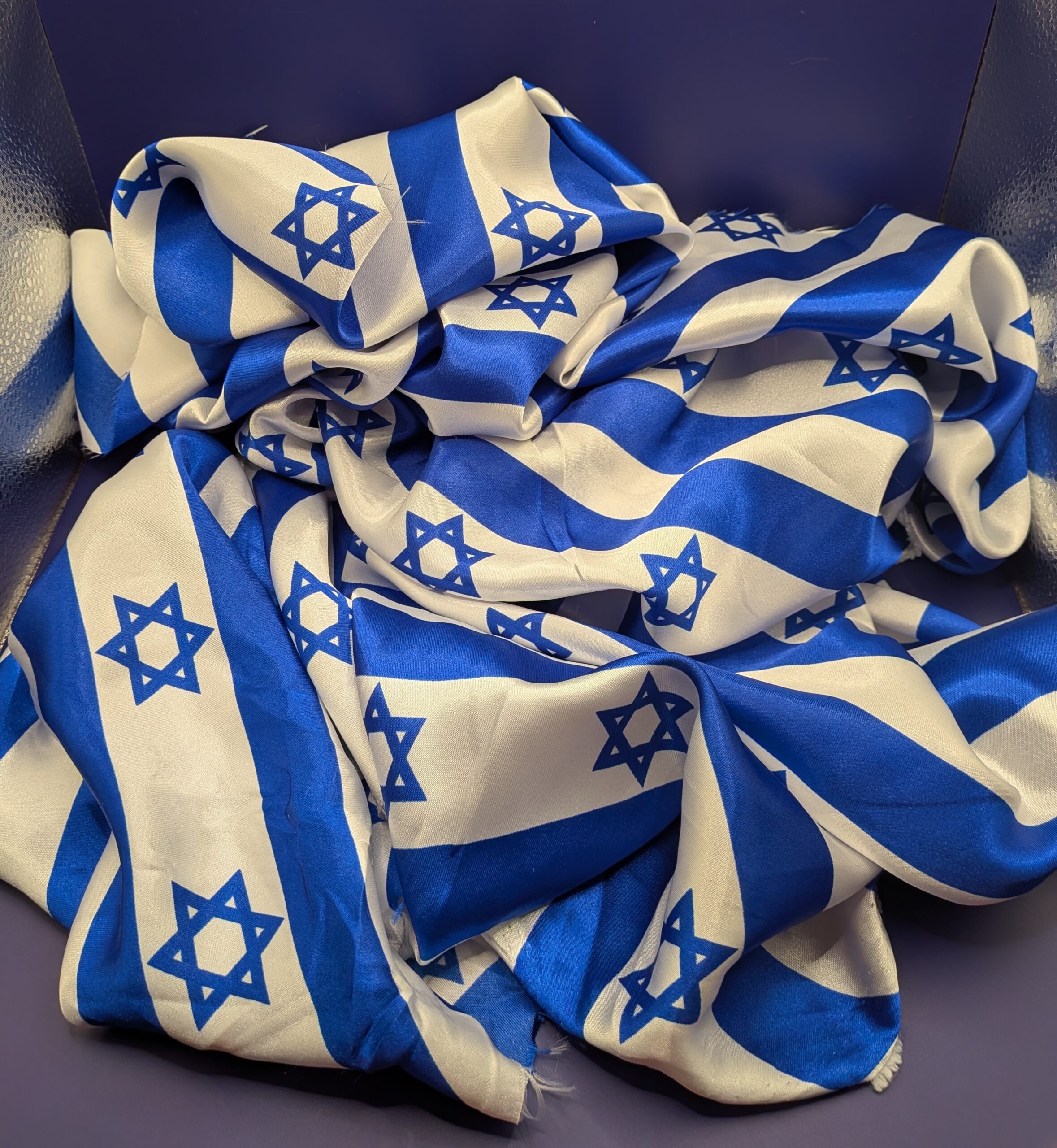 Striped Israeli flag fabric. The fabric is unfolded and scrunched up into a pile.